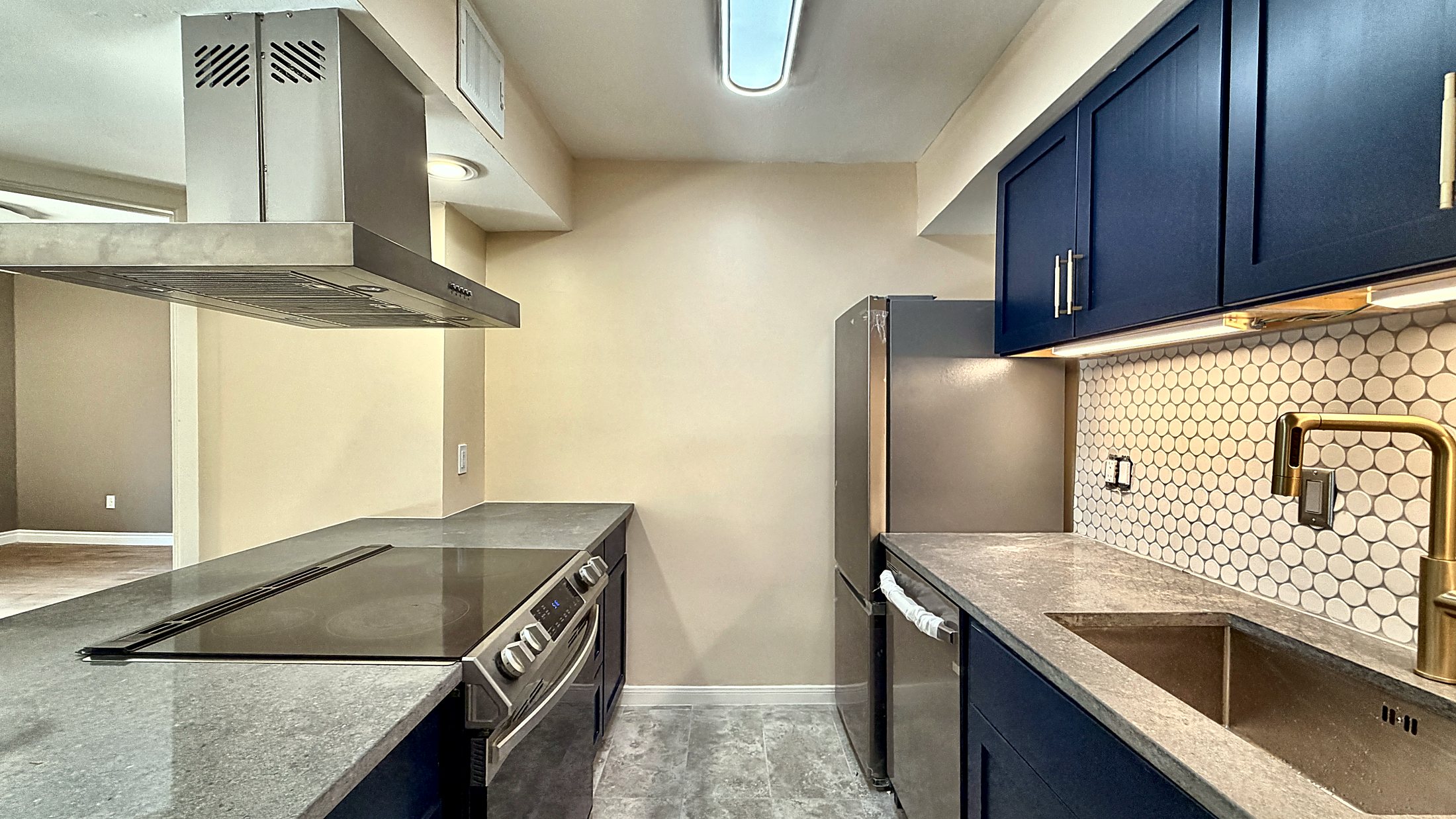 Galley kitchen at 8419 Hearth Dr seen from the entry — navy cabinets, quartz counters, new stainless appliances